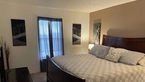 Un dormitorio con cama, mesita de noche, cómoda y ventana con cortinas.