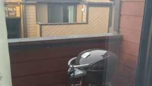 Un balcón con una parrilla, suelo de madera y vista a edificios al fondo.