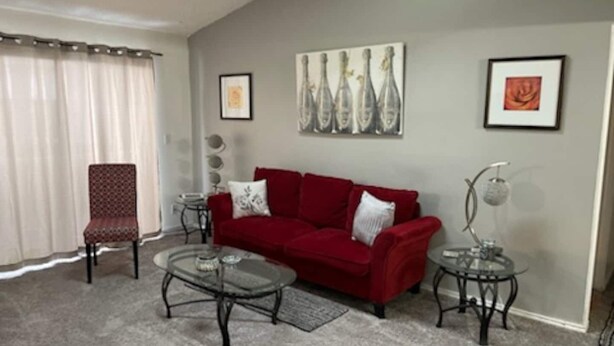 Una sala de estar con un sofá rojo, una mesa de centro de vidrio, una silla y una mesita auxiliar con una lámpara.