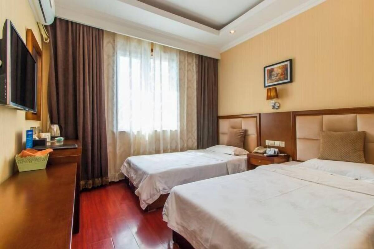 A hotel room with two beds, a television, a desk, and a window with curtains.
