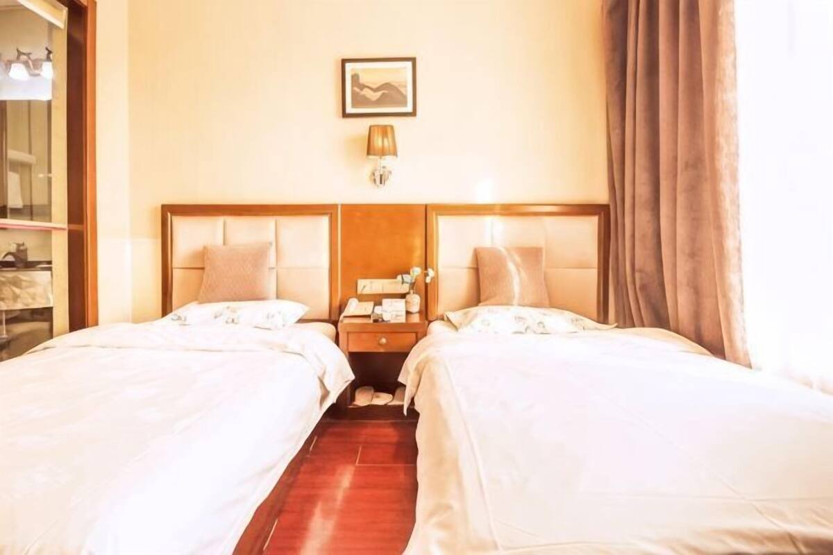 A hotel room with two beds, a nightstand, a lamp, a framed picture on the wall, and a window with curtains.