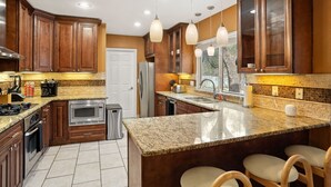 A modern kitchen with granite countertops, wooden cabinets, stainless steel appliances, and pendant lighting. - Ultimate Retreat 5-bed, Pool, Hot Tub, Mini Golf, Game Room, Playground and More (San Antonio)