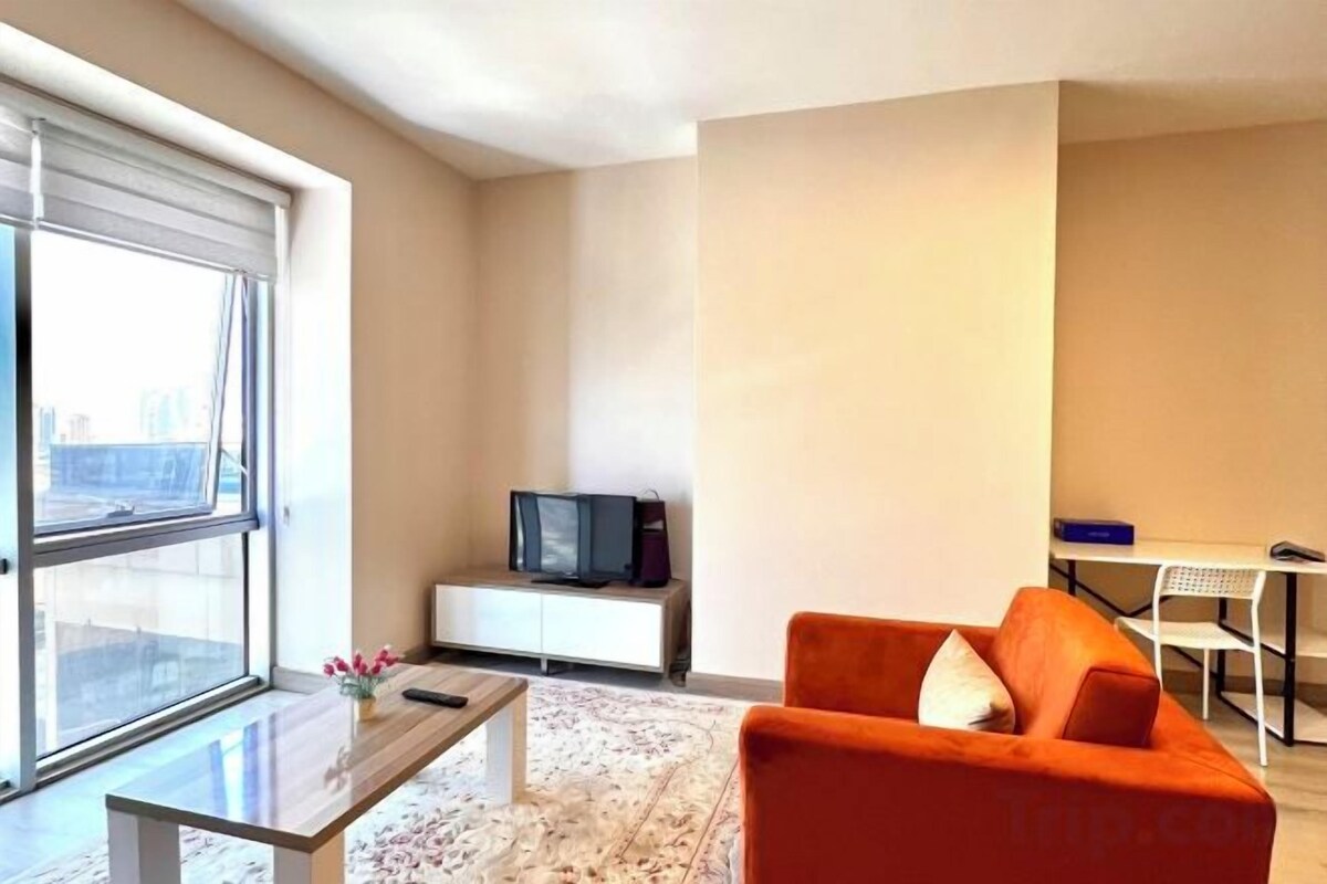 A modern living room with a sofa, a coffee table, a TV, and a view through a large window.