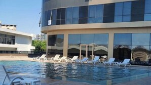 Una piscina con sillas de descanso y un edificio moderno con ventanas amplias.