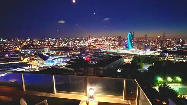 A rooftop terrace with a table, chairs, and a view of a cityscape at night. - MODERN APARTMENT (Istanbul)