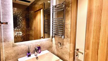 A modern bathroom with a large mirror, a white sink, a towel rack, and a wooden door.
