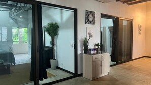 A modern interior with a sliding glass door leading to a balcony, a white cabinet with a plant, and a clock on the wall. - Beachfront 2nd level townhome. (Santa Cecilia)