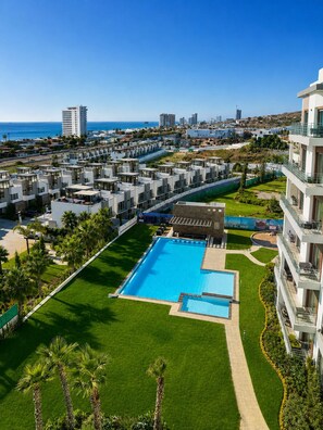 Un complex turístic amb una piscina central, edificis de diversos pisos i vistes a l'oceà.