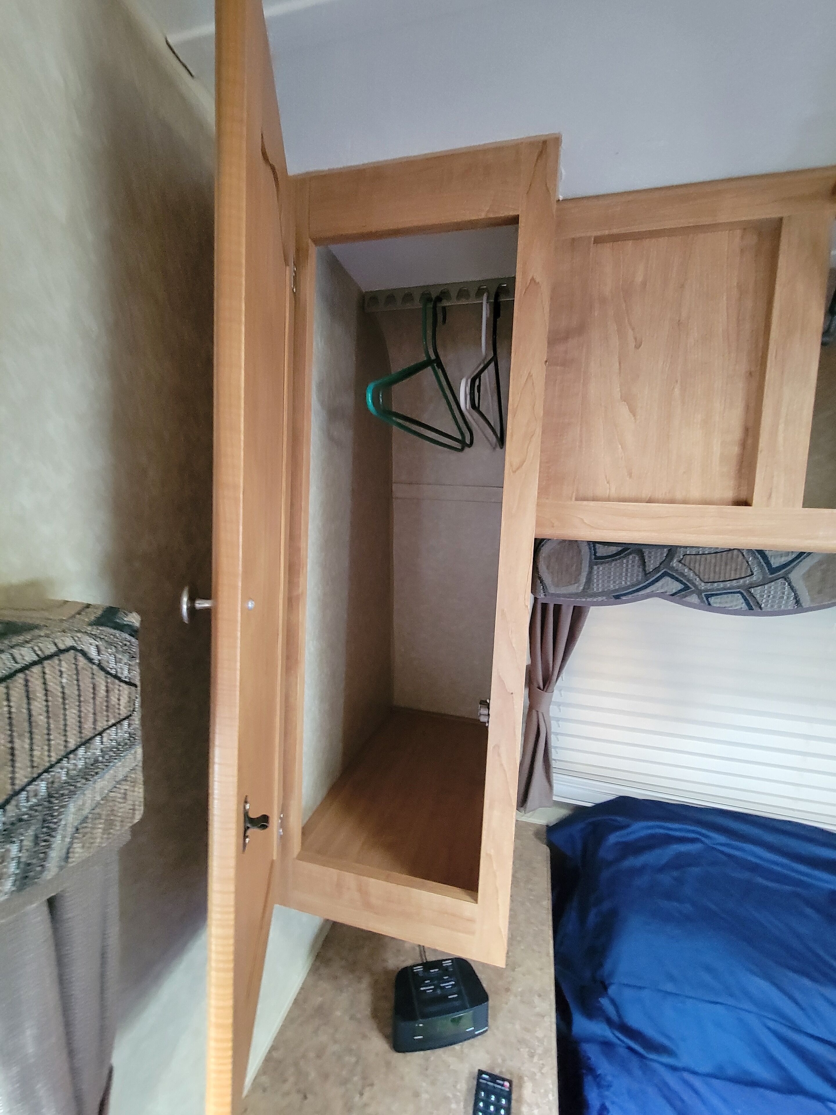 Una habitación con un armario de madera, una cama con cubierta azul y un pequeño dispositivo electrónico negro en el suelo.