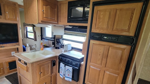 A compact RV kitchen with wooden cabinets, a microwave, a stove, and a sink.