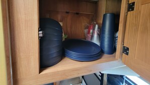 A wooden cabinet with stacked plates and a large black container.