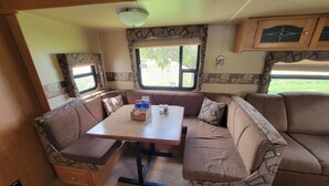 A cozy RV interior with a dining area, cushioned seating, and a window providing a view of the outdoors.