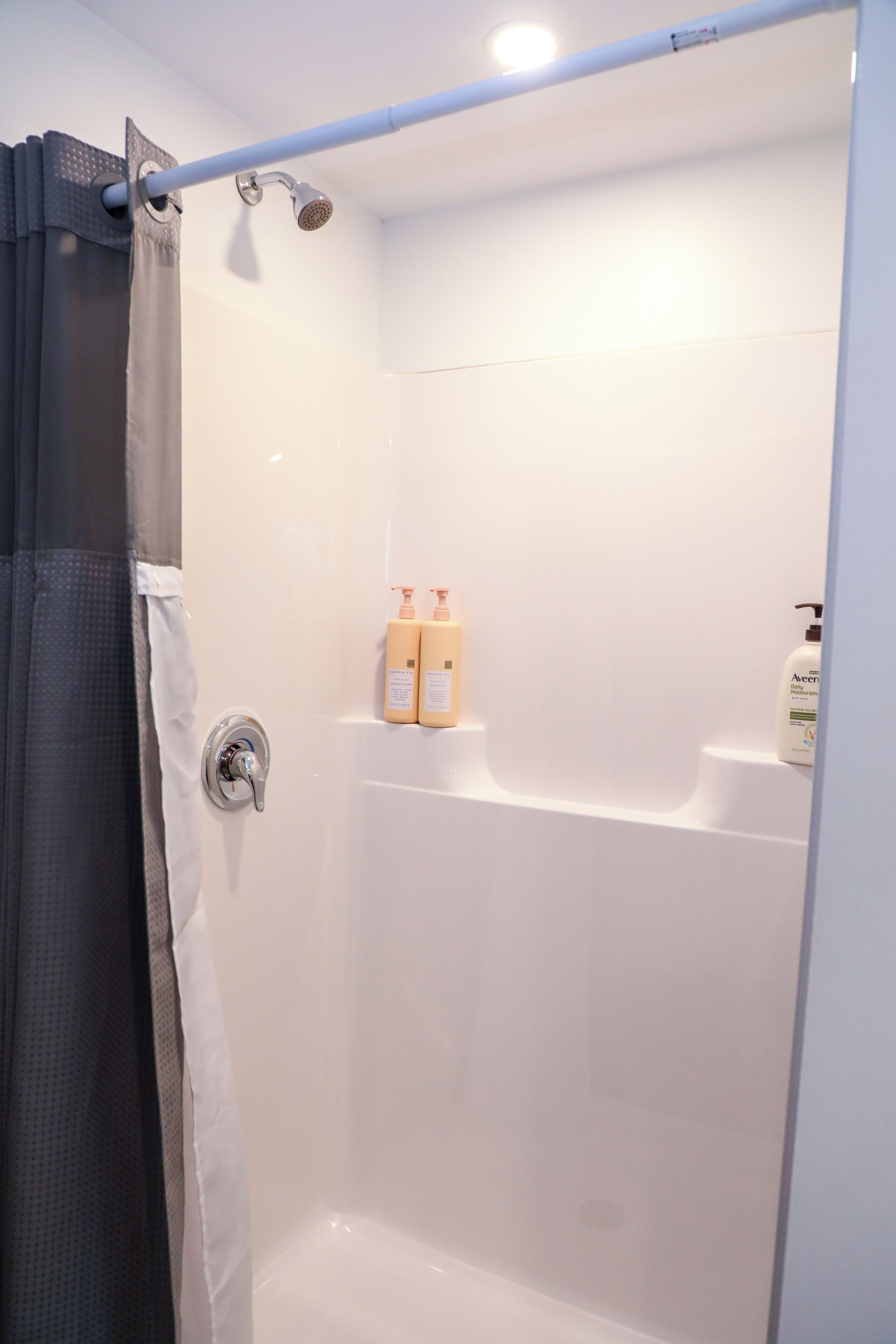 A shower with a curtain, a handheld showerhead, and two bottles of lotion on a shelf.