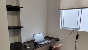 Een kleine, netjes geordende kamer met een bureau, stoel en planken.