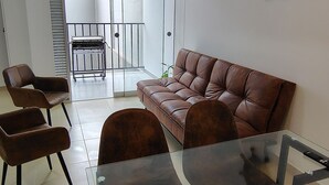 Een moderne woonkamer met een bruine leren bank, een glazen salontafel en bijpassende stoelen. Op de muur hangt een decoratieve scheepshoeveel.