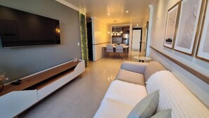 Un salon moderne avec un téléviseur à écran plat, un canapé et un coin repas à l’arrière-plan.