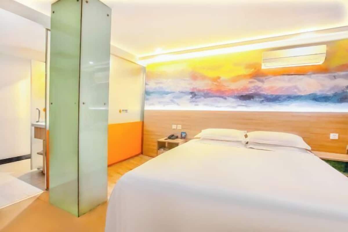 A hotel room with a bed, a nightstand, a wall-mounted air conditioning unit, and a glass partition.