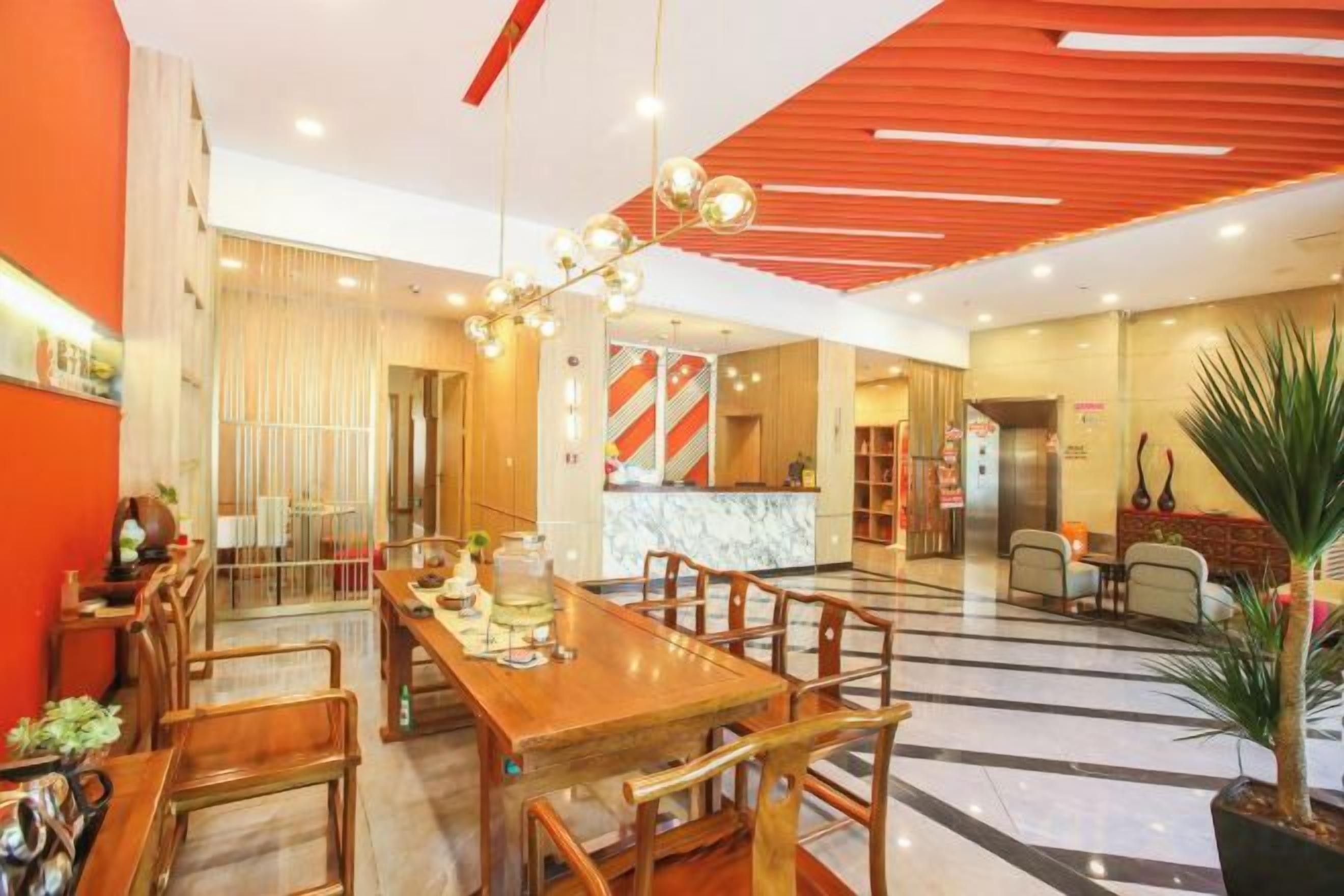 A hotel lobby with a wooden reception desk, seating area, and a large chandelier.