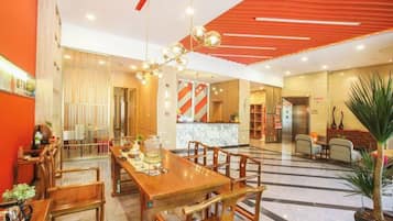 A hotel lobby with a wooden reception desk, seating area, and a large chandelier.