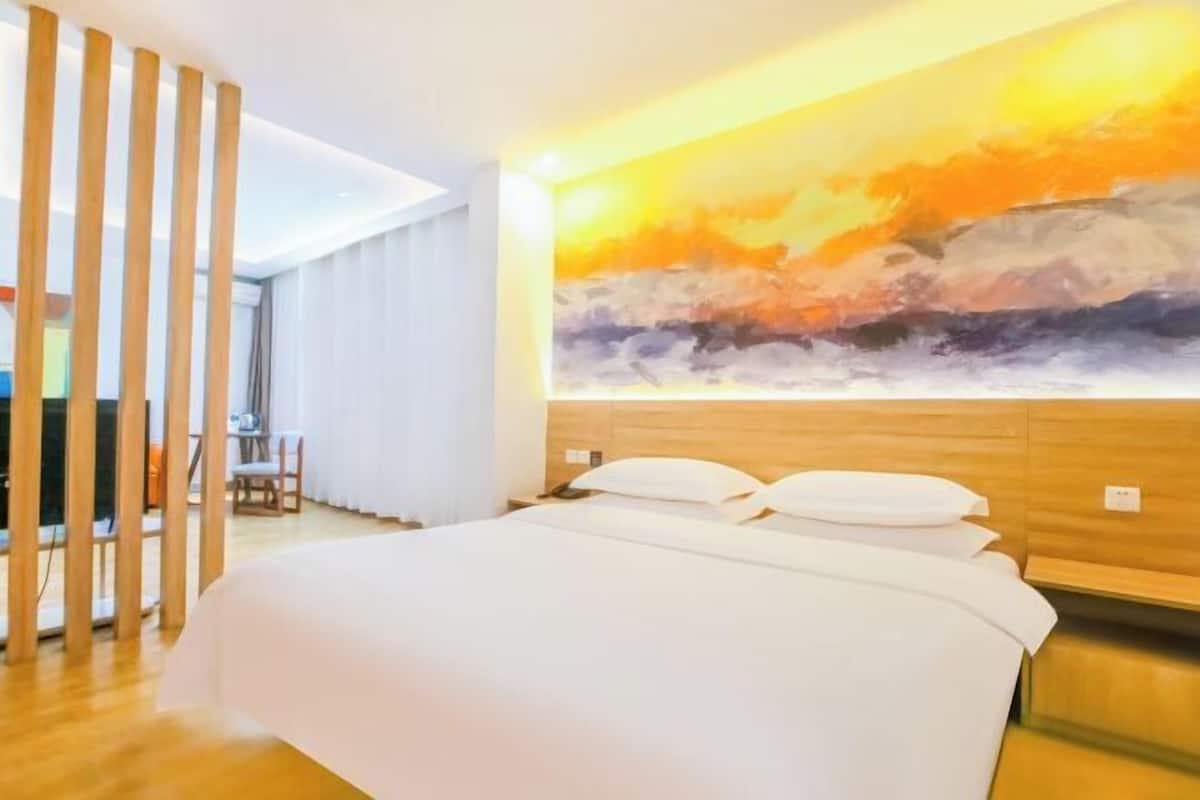 A hotel room with a bed, a painting on the wall, and a wooden partition.