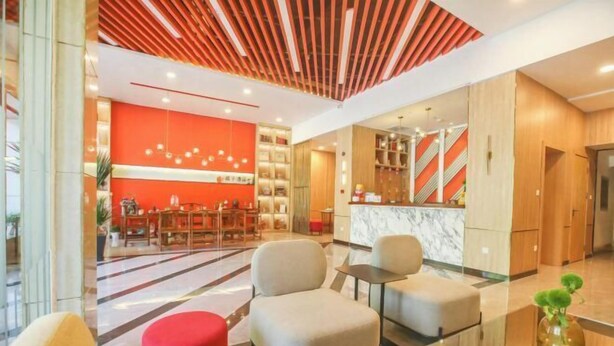 A hotel lobby with a red accent wall, a reception desk, seating area, and a modern kitchen in the background. - Orange Hotel (Taiyuan Qinxian North Street Maoye Tiandi Branch) (Taiyuan)