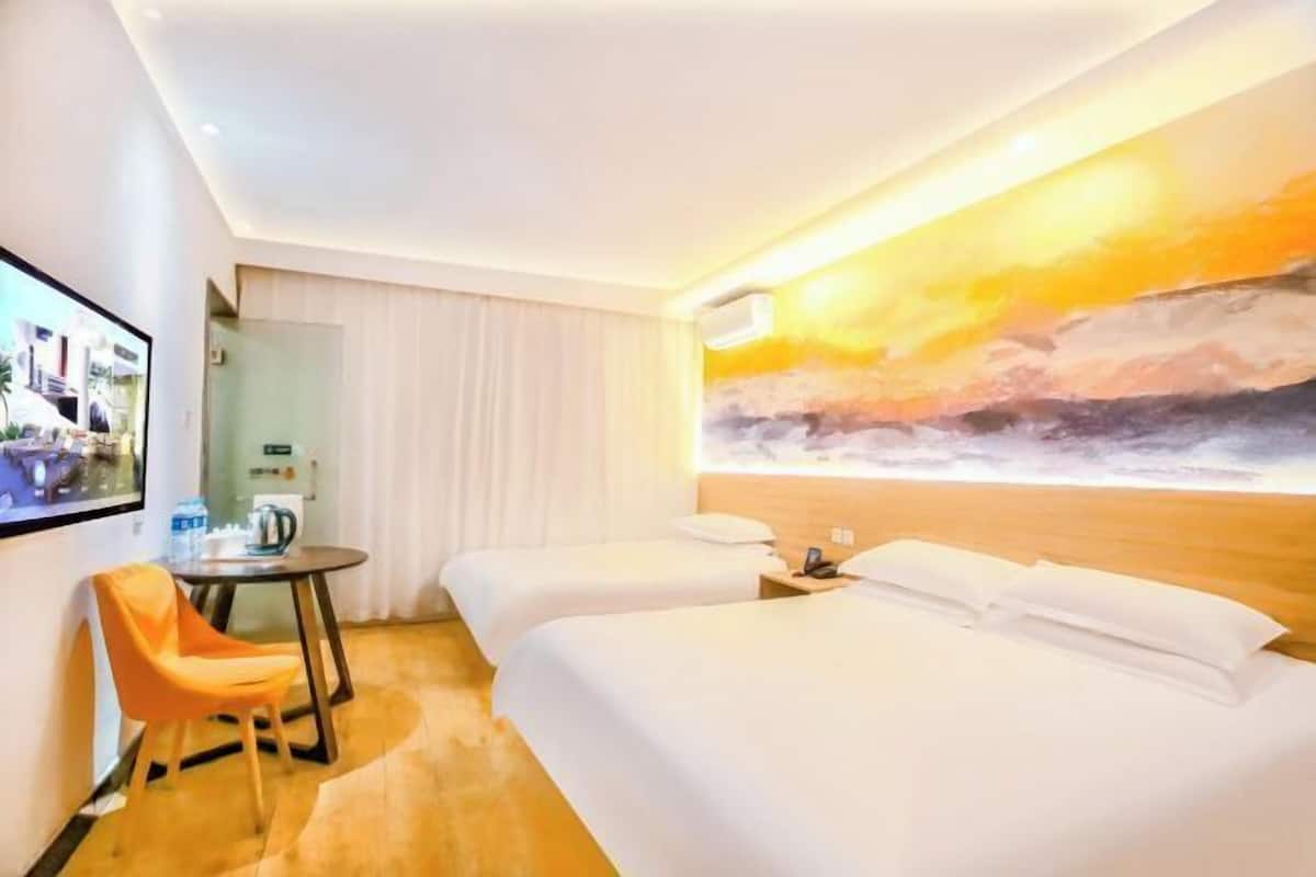 A hotel room with two beds, a TV, a small table with a chair, and a painting of a sunset on the wall.