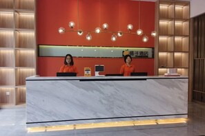 A hotel reception desk with a marble counter, two receptionists, and a modern light fixture. - Orange Hotel (Taiyuan Qinxian North Street Maoye Tiandi Branch) (Taiyuan)