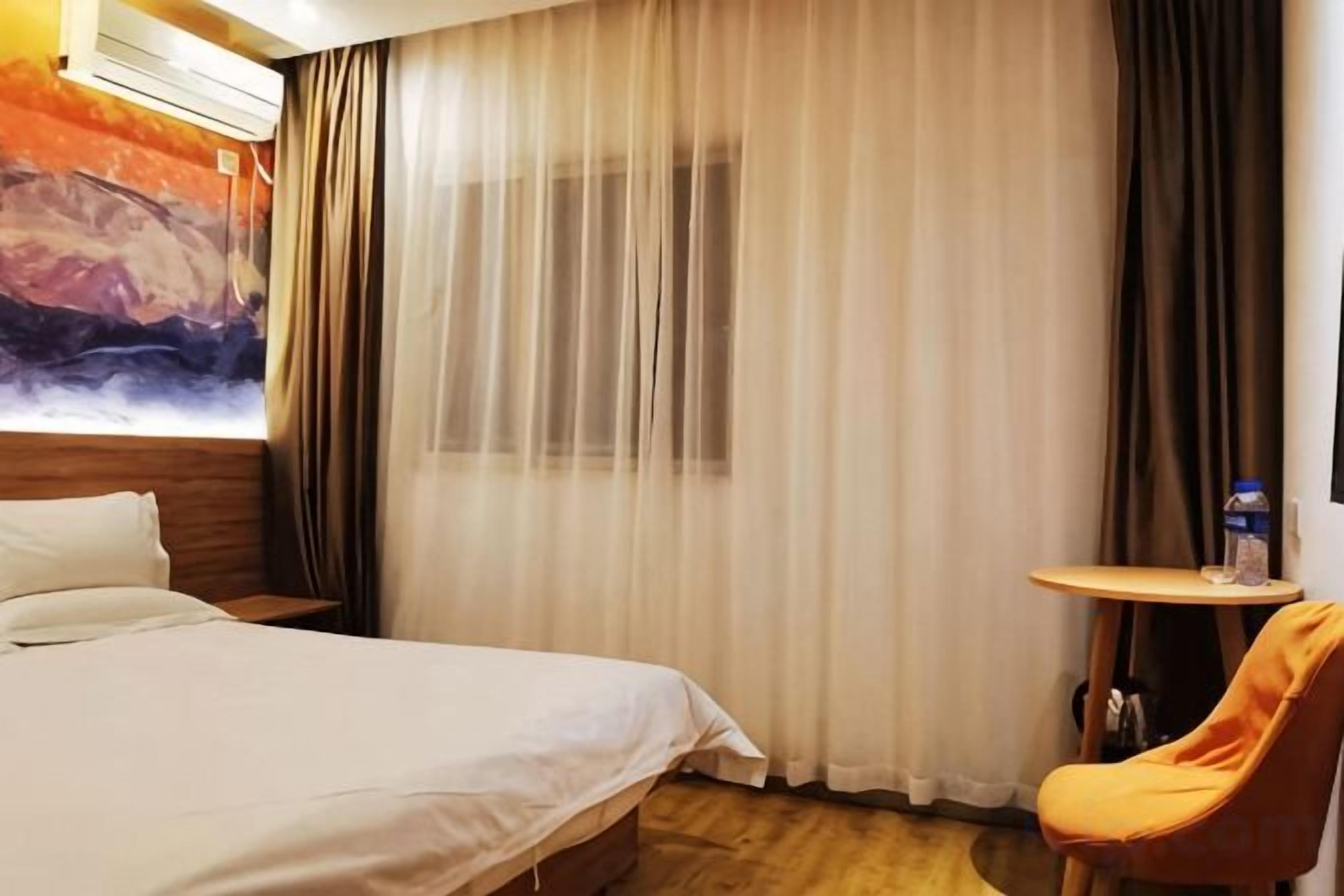A hotel room with a bed, a small table, a chair, and a painting on the wall.