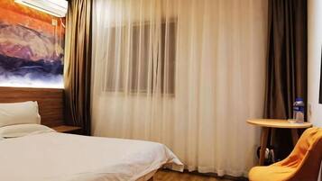 A hotel room with a bed, a small table, a chair, and a painting on the wall.