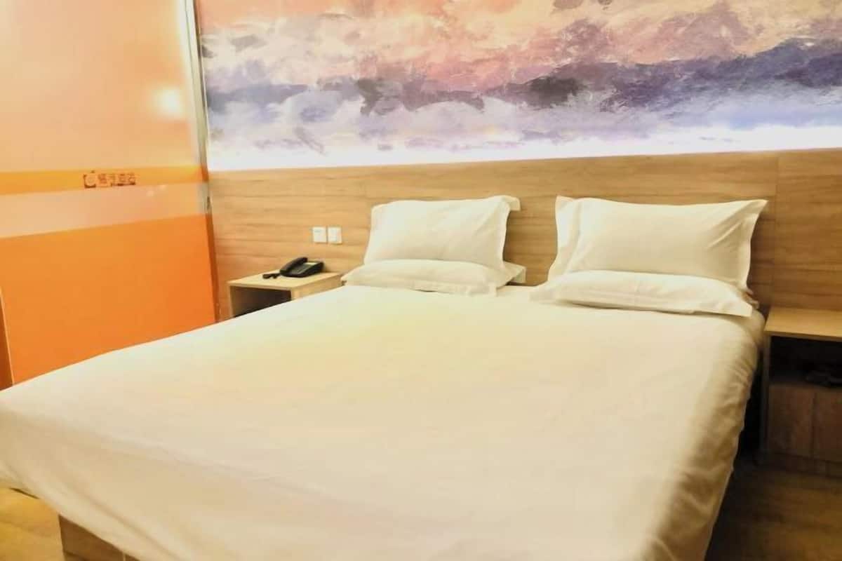 A hotel room with a large bed, two pillows, a nightstand with a phone, and a wall mural.