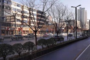 A multi-story building with a row of shops on the ground floor, a parking lot with cars, and a sidewalk with trees. - Orange Hotel (Taiyuan Qinxian North Street Maoye Tiandi Branch) (Taiyuan)