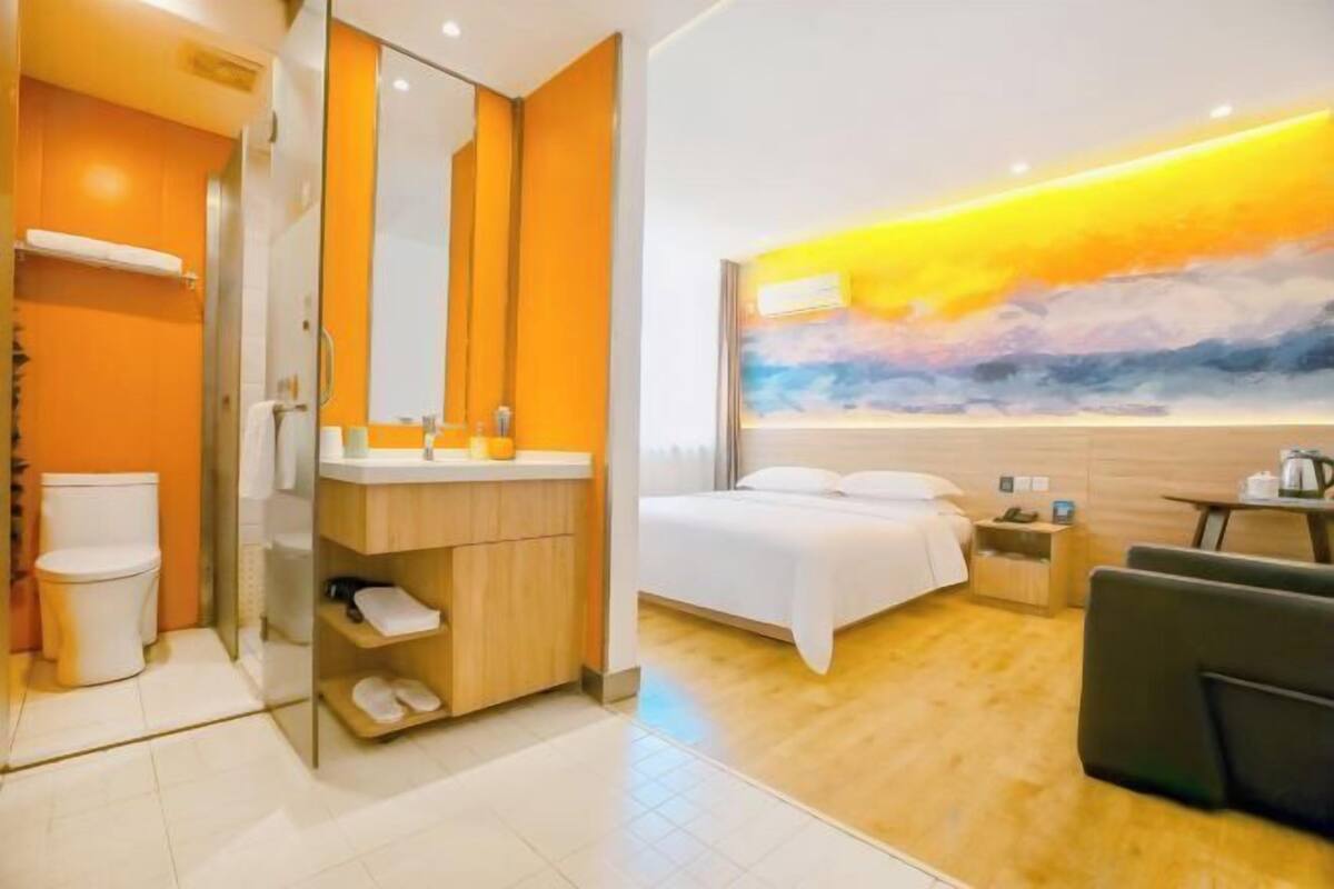 A modern hotel room with a bathroom, a bed, and a seating area.