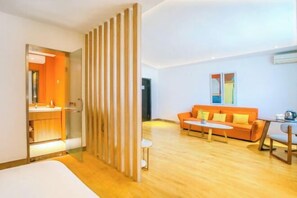 A modern hotel room with a wooden floor, a bed, an orange sofa, a small table, and a glass partition. - Orange Hotel (Taiyuan Qinxian North Street Maoye Tiandi Branch) (Taiyuan)
