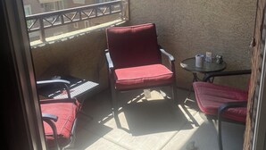 A balcony with a red chair, a small round table, and a clock on the wall. - Chic 1-bedroom apartment in fabulous Phoenix with beautiful pool and BBQs (Phoenix)
