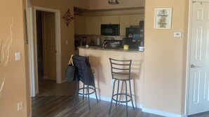 A kitchen with a microwave, refrigerator, and bar stools. There is a door on the right and a hallway leading to another room. - Chic 1-bedroom apartment in fabulous Phoenix with beautiful pool and BBQs (Phoenix)