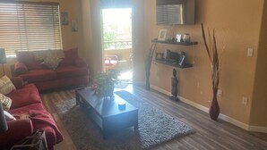 A living room with a red sofa, a coffee table, and a TV mounted on the wall. - Chic 1-bedroom apartment in fabulous Phoenix with beautiful pool and BBQs (Phoenix)
