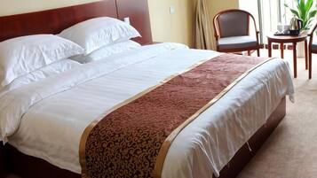 A neatly made bed with white linens and a patterned throw, a wooden headboard, and a small table with a plant beside the bed.