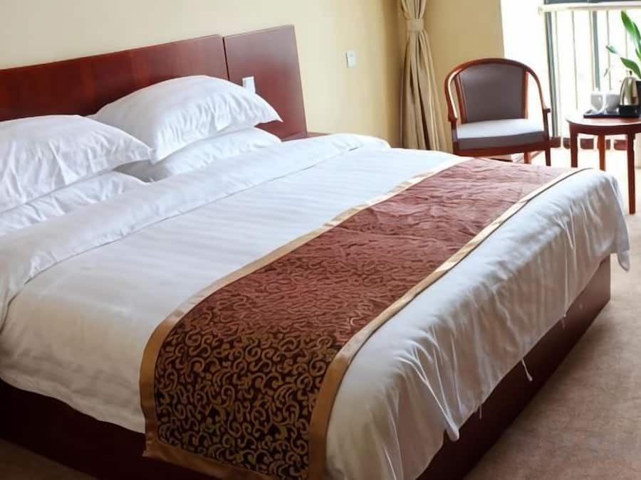 Ein ordentlich bezogenes Bett mit weißen Leinen und einer gemusterten Tagesdecke, ein Holz-Kopfteil und ein kleiner Tisch mit einer Pflanze daneben.
