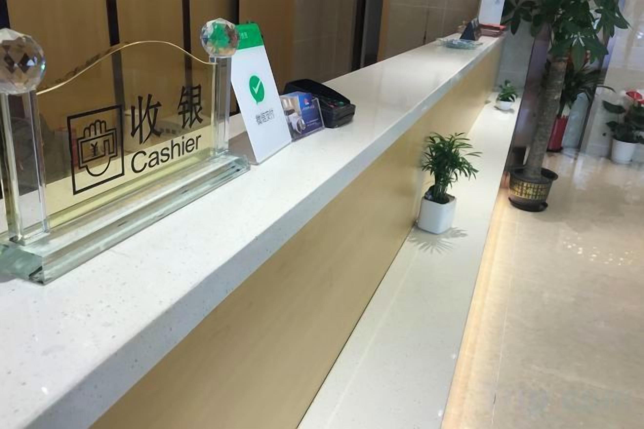 A reception desk with a cash register, a plant, and a small potted plant on the counter.