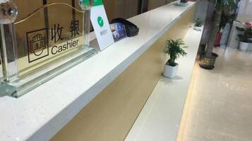 A reception desk with a cash register, a plant, and a small potted plant on the counter.