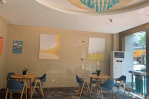 Un hall de hotel con mesas y sillas redondas, obras de arte en las paredes y un equipo de aire acondicionado grande.