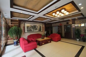 A lobby with a large potted plant, red seating, a wooden coffee table, and a framed artwork on the wall. - Baotai Business Hotel (Shanghai Wusong International Cruise Terminal Songbin Road Subway Station) (Shanghai)