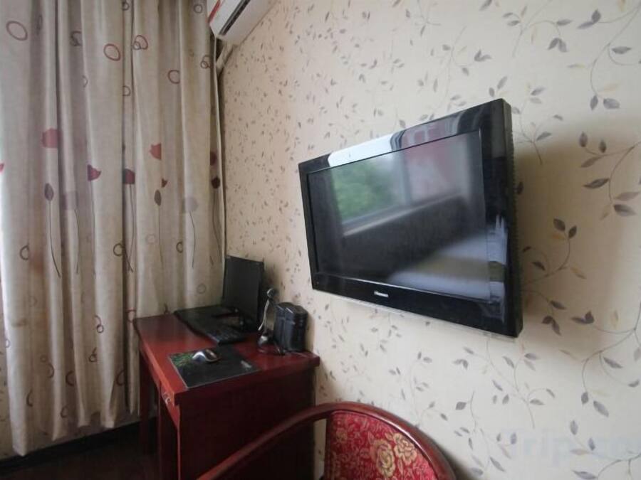 A room with a flat-screen TV mounted on the wall, a wooden desk with a computer, and a red chair.