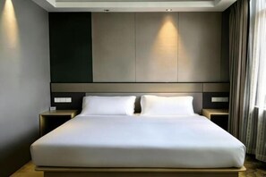 Una habitación de hotel moderna con una cama grande, dos mesitas de noche y una paleta de colores neutros.