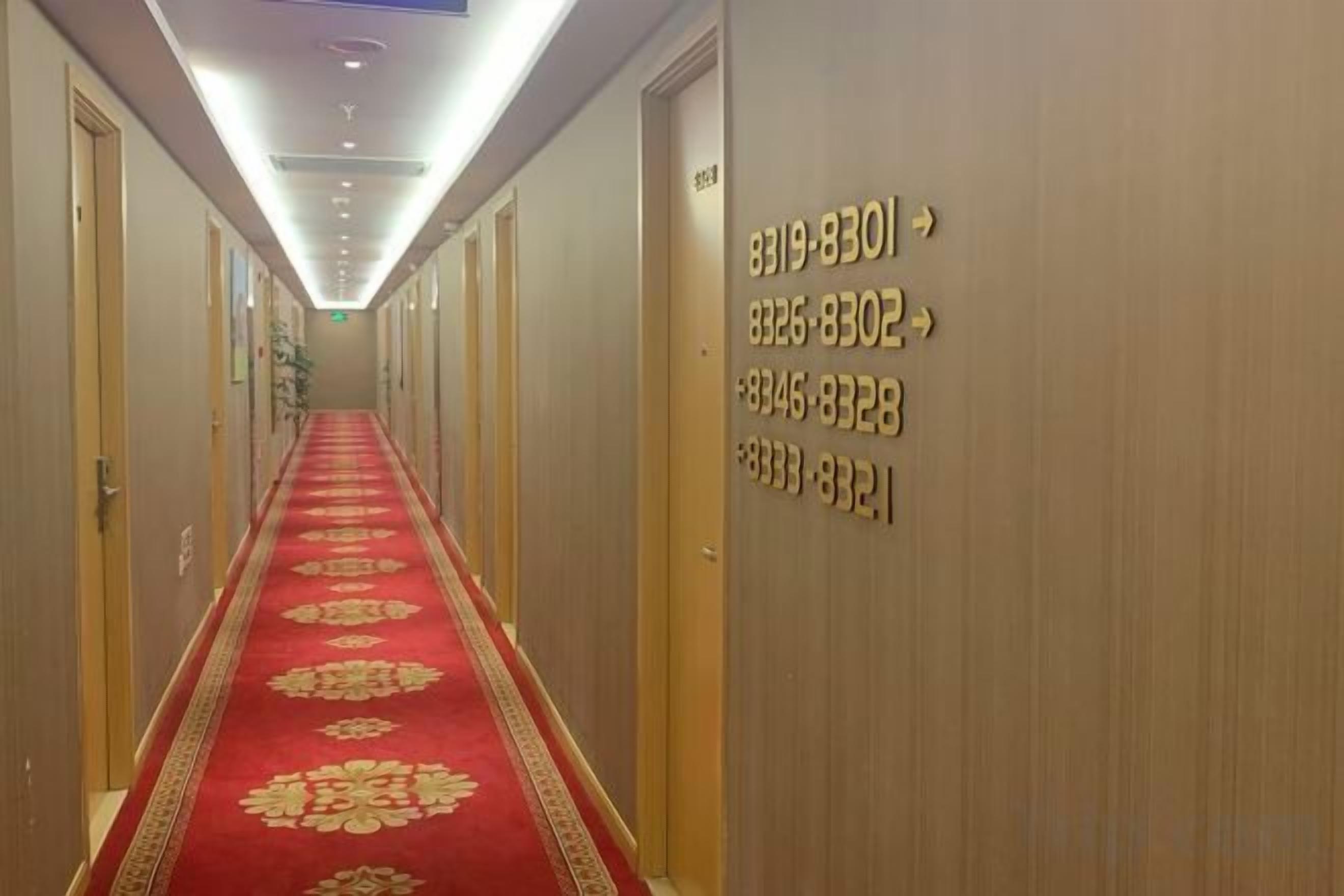 Corredor de hotel com carpete vermelho, portas numeradas e iluminação embutida no teto.