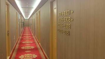 Corredor de hotel com carpete vermelho, portas numeradas e iluminação embutida no teto.
