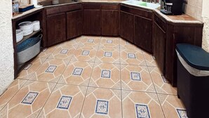 Une cuisine de taille modeste, dotée de meubles en bois foncé, d’un îlot central et d’un sol carrelé à motifs.