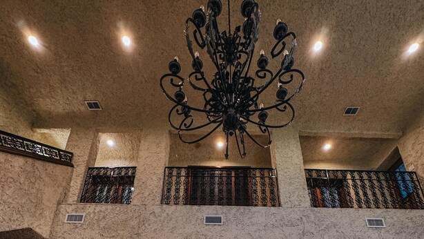 Un hall d’entrée agrémenté d’un lustre, de fauteuils à motifs rouges, d’une table basse en marbre et, au fond, d’un espace repas.