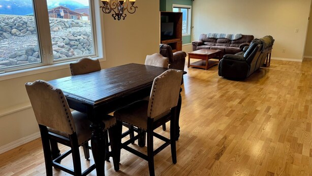 A dining area with a wooden table and chairs, a chandelier, and a view of a rocky landscape through a large window.