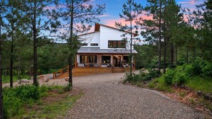 A modern two-story house with a covered porch, surrounded by a forested area.